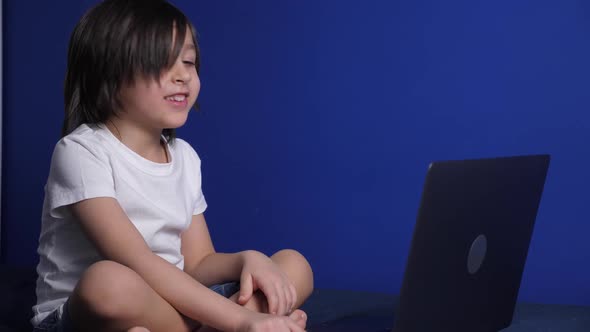 Boy Child in a White Tshirt and Shorts is Sitting on a Bed Against a Blue Wall of the House