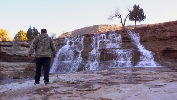 Man walking towards waterfall in desert landscape