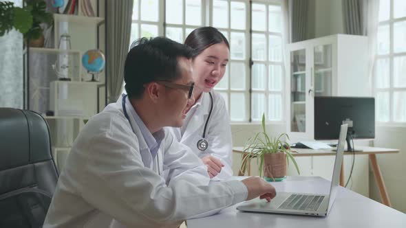 Two Asian Professional Physicians Talking, Consulting And Working On Laptop Computer