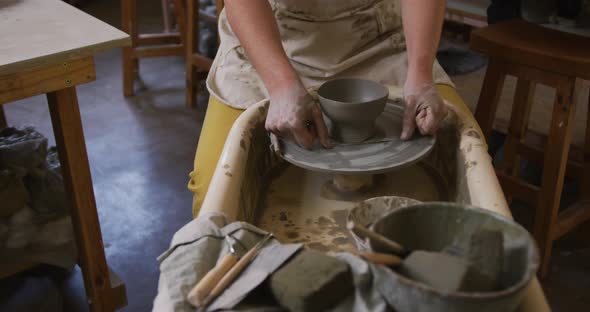 Mid section of female potter using loop tool for finishing pottery at pottery studio