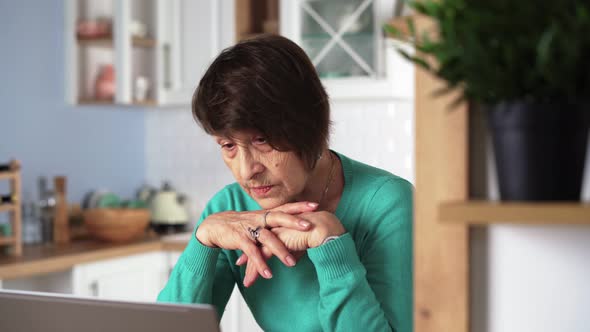 Elderly Woman Laughing and Smiling Using Laptop at Home in Kitchen