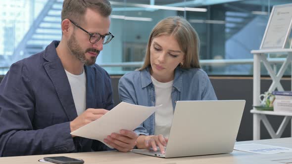 Businessman and Businesswoman Reading Documents While Using Laptop