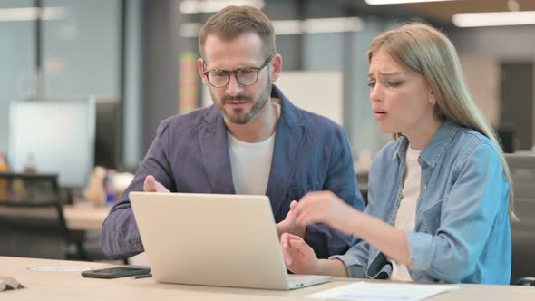 Businessman and Businesswoman Reacting to Loss on Laptop in Office