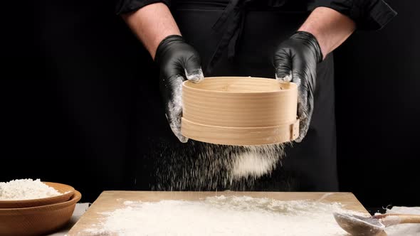 chef in black latex gloves and black clothes holds a round wooden sieve