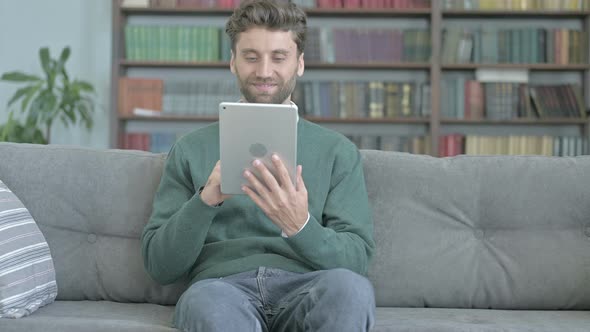 Happy Man Video Calling on Tablet While Sitting on Sofa