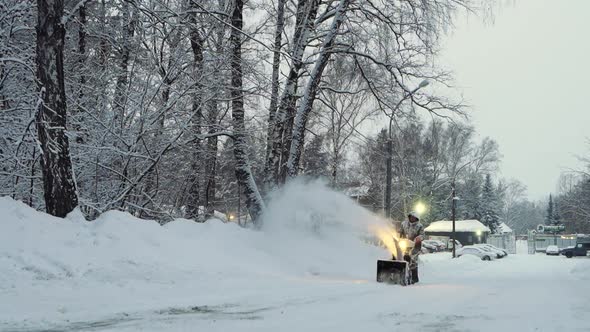 Snowcovered Man Cleans the Road in Winter with Blower Snow Removal Equipment