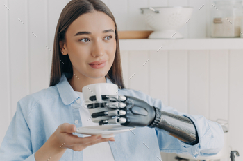 A young woman with a bionic prosthetic hand admiringly holds a cup, a merger of humanity