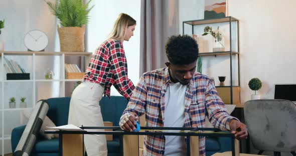 Girl Gethering Cardboard Boxes on the Sofa while Positive Confident  Guy Measuring Folded Rack