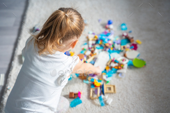 Little girl play with constructor toy on floor in home living room, educational game, spending