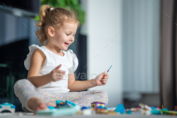 Happy little girl playing with small constructor toy on floor in home, educational game, spending