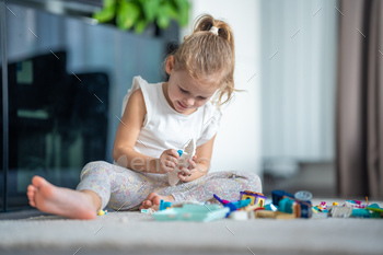 Smiling Little girl playing with small constructor toy on floor in home, educational game, spending