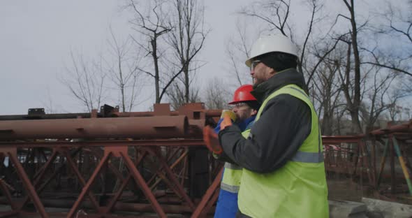 Male Bridge Builders Walking and Talking Near Metal Structures