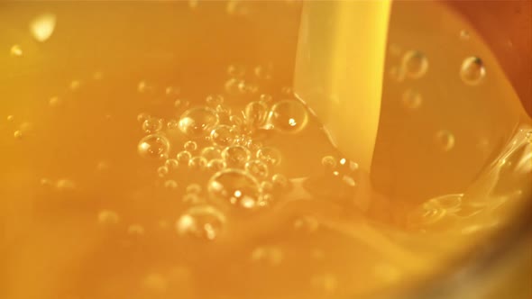 A Stream of Orange Juice Pours Into a Glass with Air Bubbles