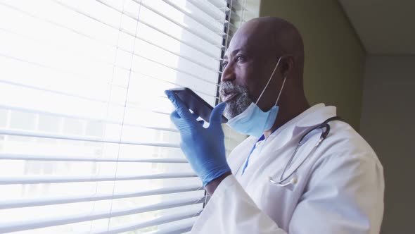 Portrait of african american male doctor wearing face mask talking using smartphone