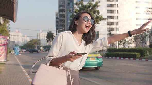 young Asia businesswoman hailing on road catching taxi and holding smart phone while.