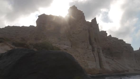 Tracking shot of white volcanic cliffs at a black sand beach on the island of Santorini, Greece.