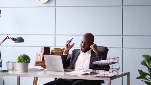 Afroamerican Businessman Talking on Phone with Client Looking at Laptop Screen Working From Home