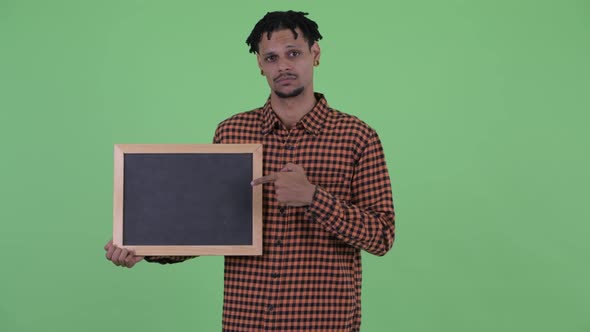 Serious Young African Man Holding Blackboard and Giving Thumbs Down