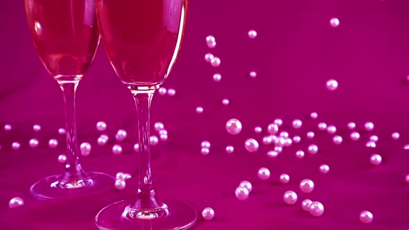 Falling white pearls next to wine glasses on a purple background. Slow motion.