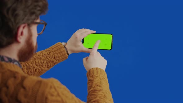 Caucasian Man in His 30s Scrolling and Touching His Smartphone with Green Mockup Screen Over the