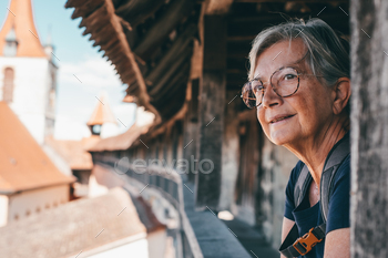 Senior woman with eyeglasses and backpack looking away from the balcony of an ancient home
