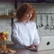 Redhead Young Woman with Curly Hair Sit at Table in Cozy Kitchen Working at Laptop Computer - VideoHive Item for Sale