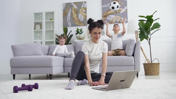 Young Brunette in Training Clothes which Sitting on the Floor in Front of the Computer