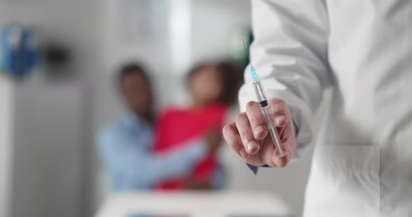 Close Up of Doctor Holding Syringe with Covid19 Vaccine and Parent Holding Child on Blurred