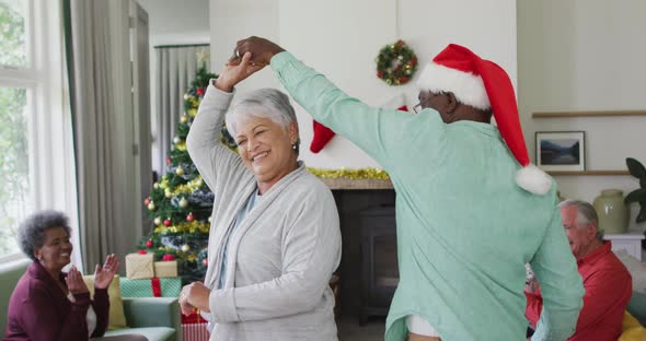 Happy diverse senior couple dancing together with friends in background at christmas time