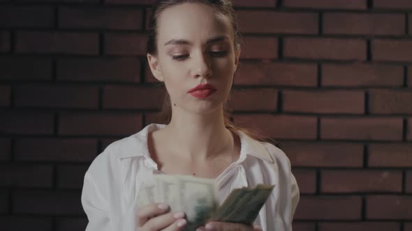 Serious Woman Counting Money Banknotes on Brick Wall
