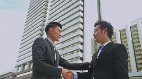 Asian businessmen partnership making handshake in the city with highrise building in background.