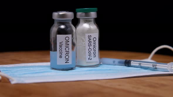 Two vials of Omicron vaccine, a syringe and a medical mask on a wooden background