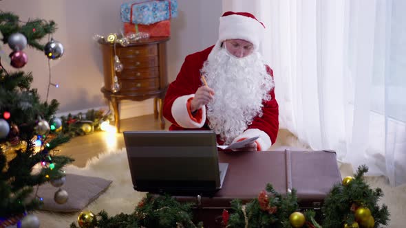 Front View Santa Clause Signing Envelope with Letter Sitting in Living Room Indoors