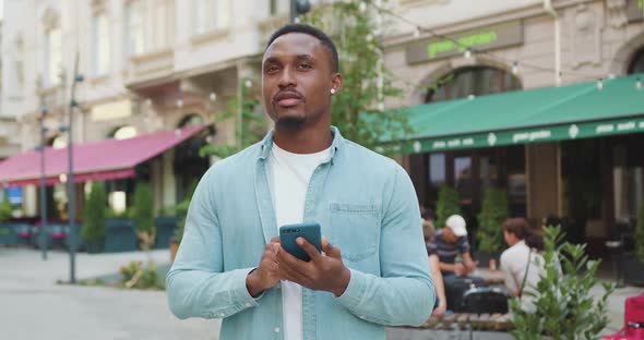 Man in Casual Clothes which Standing Near Street Cafe and Typing Message on Phone