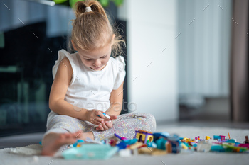 Little girl playing with small constructor toy on the floor in home, educational game, spending