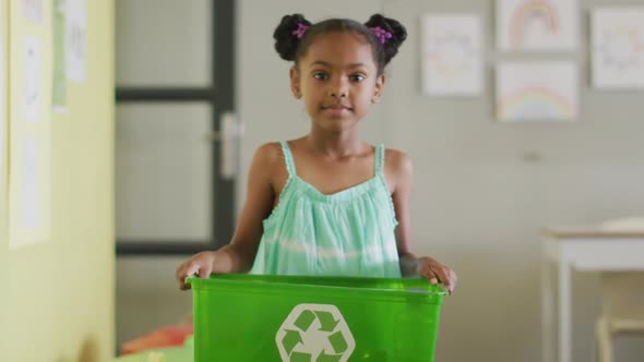 Video of happy african american girl holding box with recycling symbol in classroom