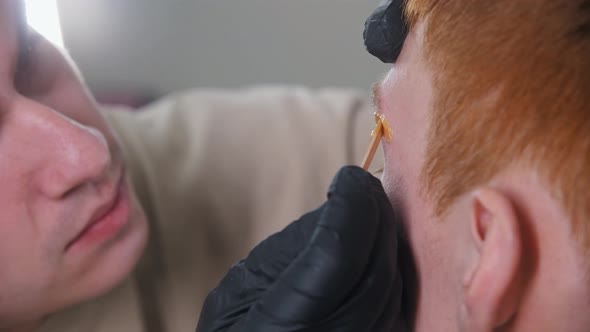 Attractive Man Brow Master Applying Wax Under the Brow of His Male Client