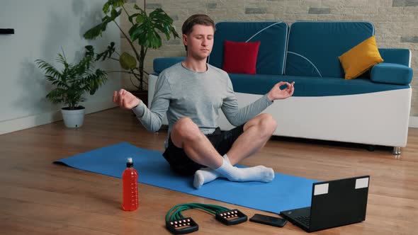 Young Guy Meditating in Lotus Pose on Exercise Mat at Home.