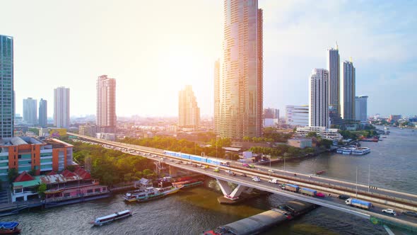 Aerial view flight over a moving sky train on a bridge over the Chao Phraya River