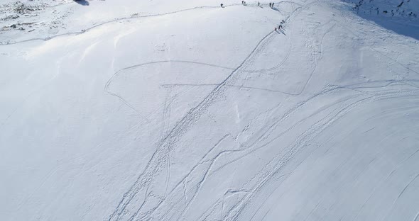 Backward Aerial Top View Over Winter Snowy Mountain Ski Track Field with People in Sunny Day