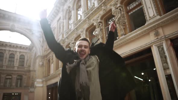 Smiling Caucasian Young Male in Street Outerwear Jumping in Beautiful Passageway in Odessa in