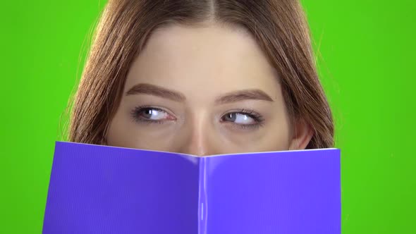 Schoolgirl Covered Her Face with a Violet Notebook . Green Screen. Close Up