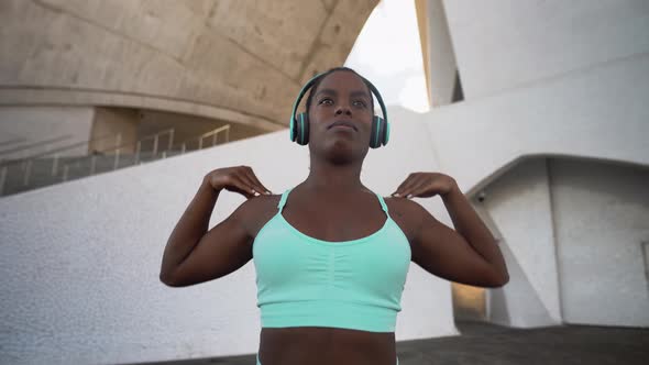 Young African fit woman listening music with headphones during workout session outdoor