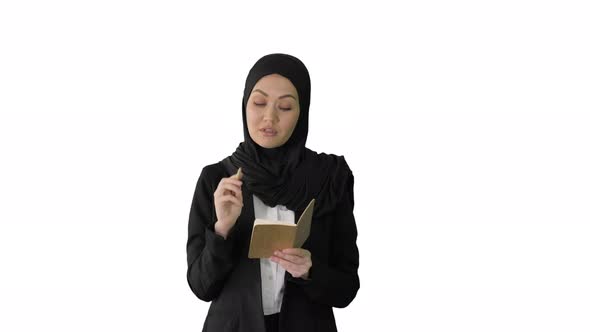 Muslim Businesswoman Thinking and Writing Ideas in Her Notepad While Walking on White Background