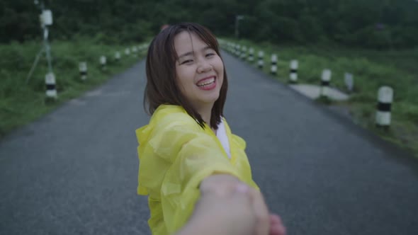 Young Asian woman feeling happy playing rain while wearing raincoat standing near lake.