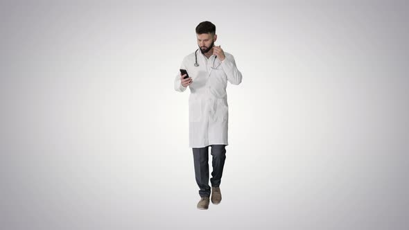 Male Doctor in White Medical Uniform Walking and Using Smartphone on Gradient Background