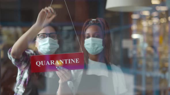 Two Waiters in Masks Hanging Quarantine Sign on Restaurant Glass Door Closing Place