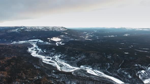 Aerial footage of black dense forest and white frozen Tetsa River in Alberta, Canada