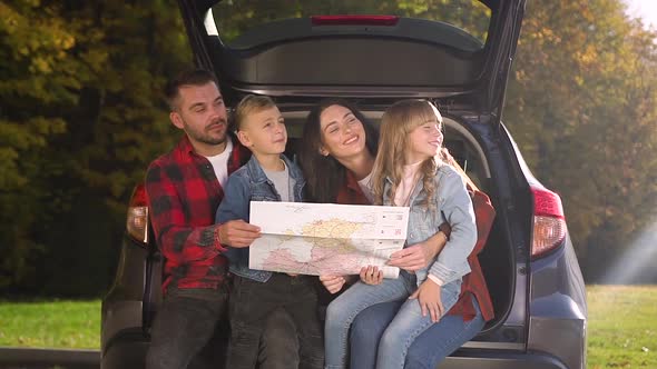 Family Sitting in the Auto's Trunk, Using the Road Map and Looking Aside