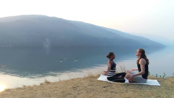 Friends performing yoga near lakeside 4k